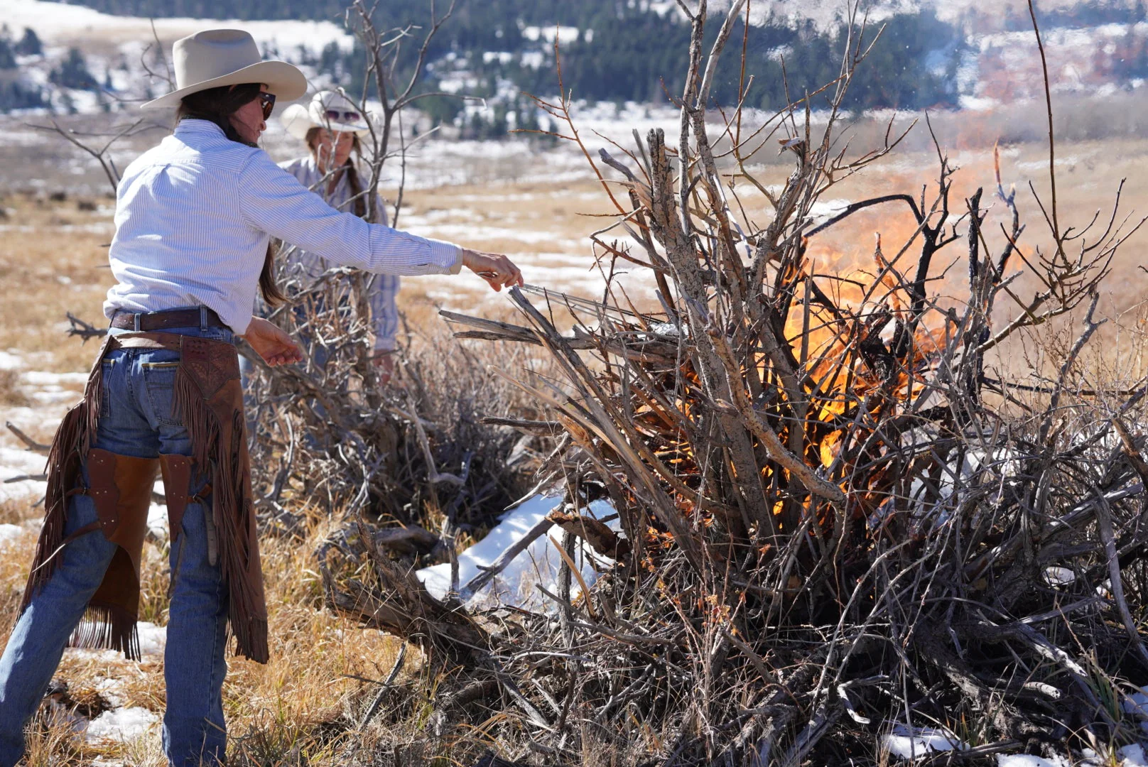 cowgirl starting a fire in a brush pile to cook a meal on