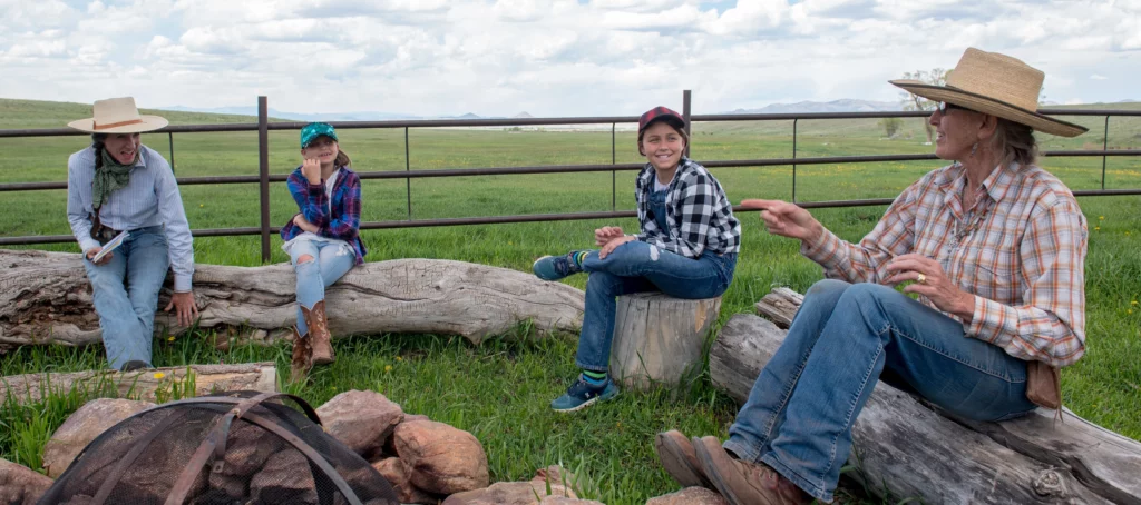 cowgirls talking with two children sitting on logs surrounded by pastures at Music Meadows Ranch