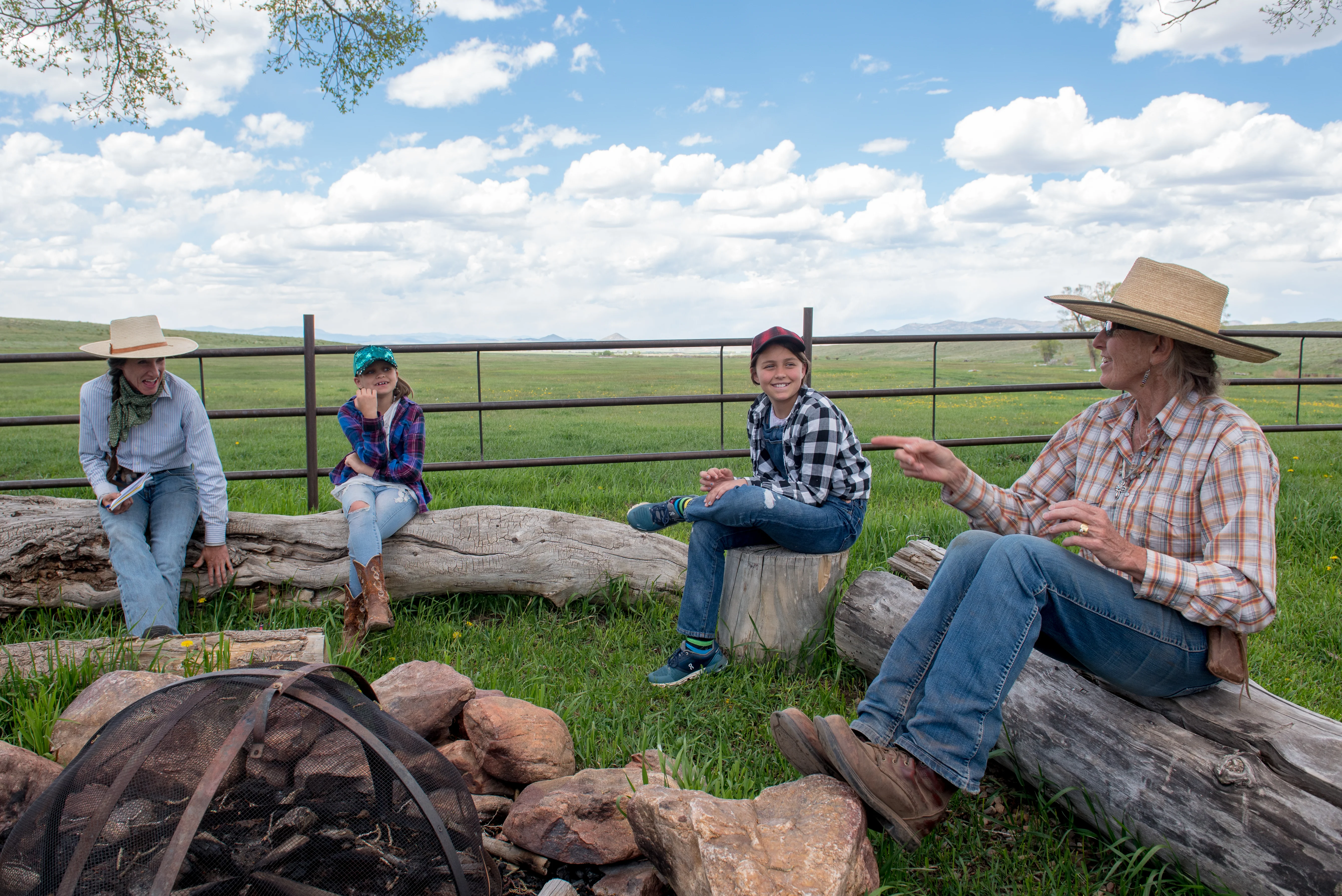 cowgirls talking with two children sitting on logs surrounded by pastures at Music Meadows Ranch