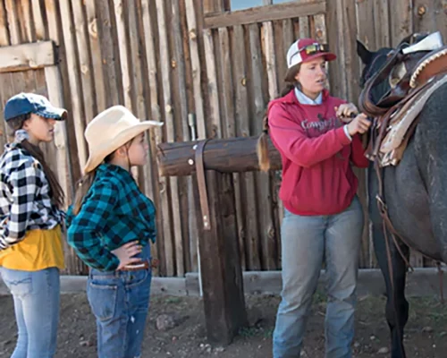 cowgirl teaching young girls how to saddle a horse properly