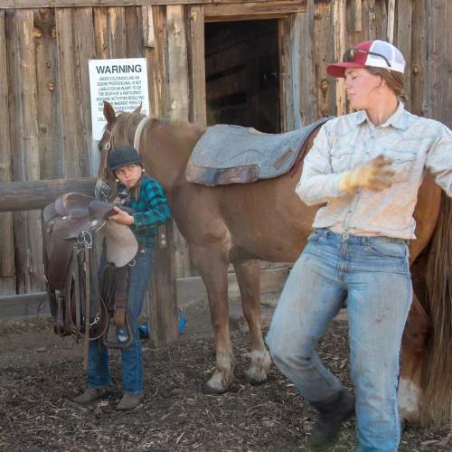 cowgirl teaching a child to saddle a horse