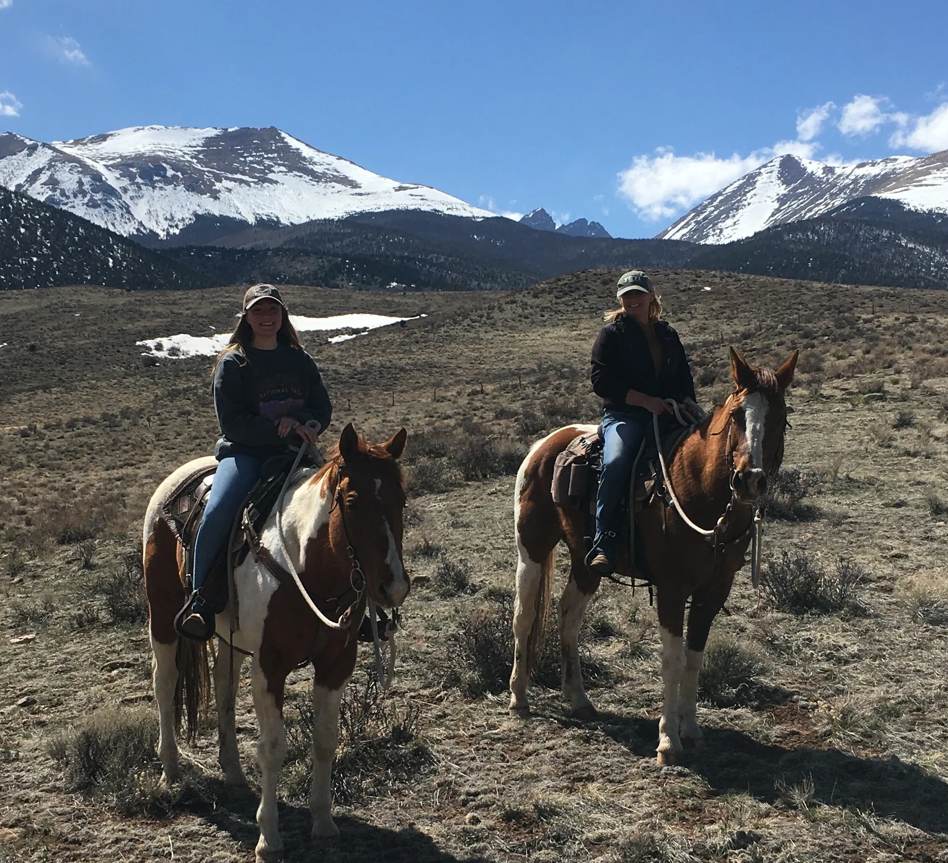two women sitting on horseback at the base of snowcapped mountains in colorado